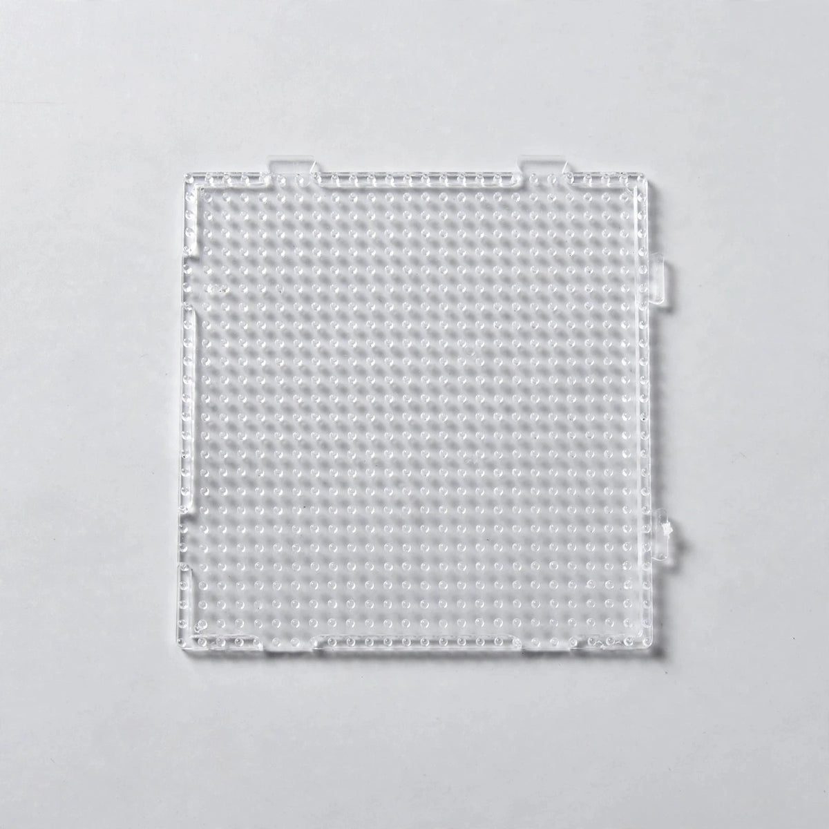 A clear square plastic bead pegboard with interlocking edge tabs is shown from above on a light grey background.