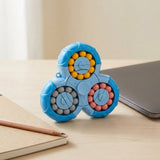 Blue plastic fidget puzzle with yellow, gray, and pink beads stands on a light wooden desk beside a laptop, notebook, and pencil.