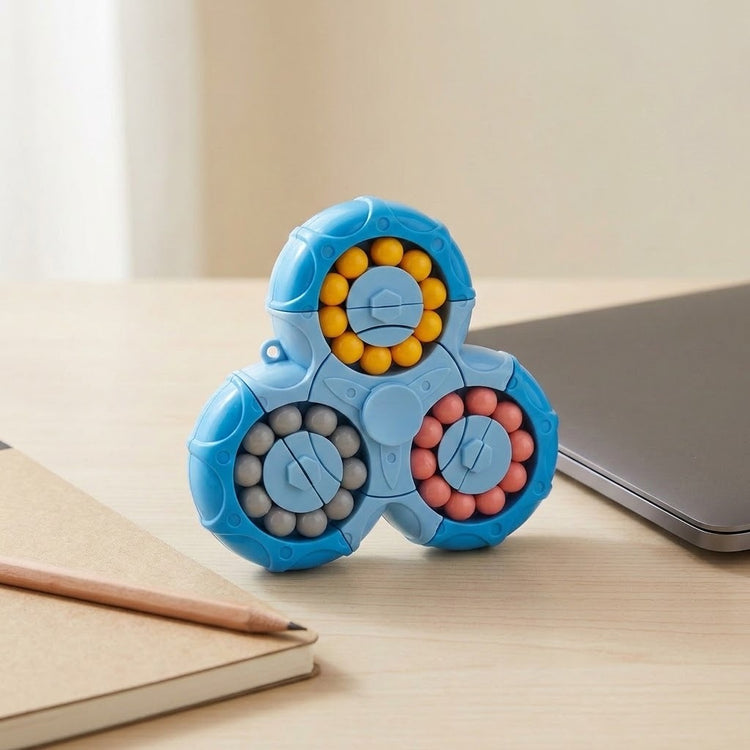 Blue plastic fidget puzzle with yellow, gray, and pink beads stands on a light wooden desk beside a laptop, notebook, and pencil.