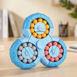 Blue plastic fidget puzzle with three circular bead tracks stands on a wooden desk with blurred books and stationery behind it.