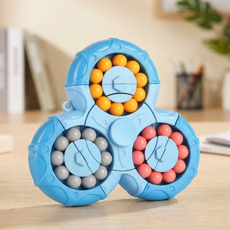 Blue plastic fidget puzzle with three circular bead tracks stands on a wooden desk with blurred books and stationery behind it.