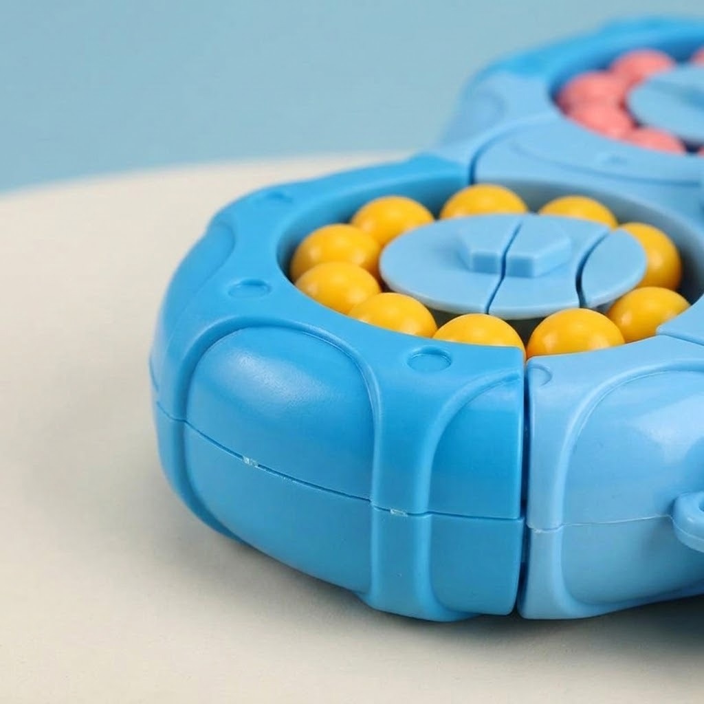 Close-up of a blue plastic fidget puzzle shows yellow beads, a circular rotating section, and molded edges on a pale surface.