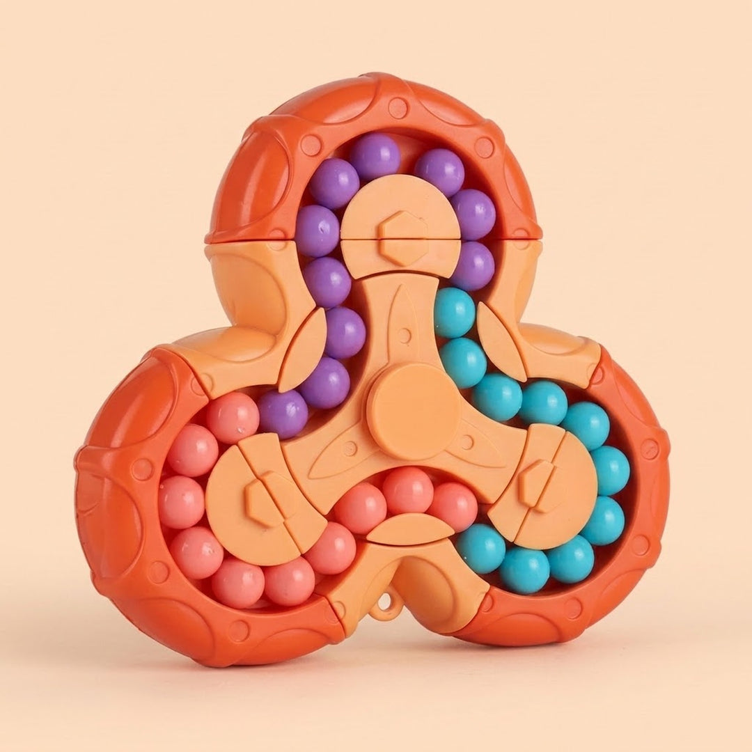 A three-spoke fidget puzzle toy with orange plastic outer rings, peach-colored center pieces, and rows of small round beads in purple, turquoise, and pink, shown on a warm beige background.