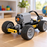 A gray MOC Power Functions motor drives a small wheeled building-block model across a play table.
