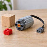 A gray MOC Power Functions motor is fitted into a small building-block train on an indoor play track.