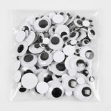 A clear plastic bag filled with many white googly eyes with black centers, photographed on a plain white background.