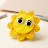 Two plastic googly eyes with black pupils and yellow eyelash details decorate a yellow sun craft on a cream surface.