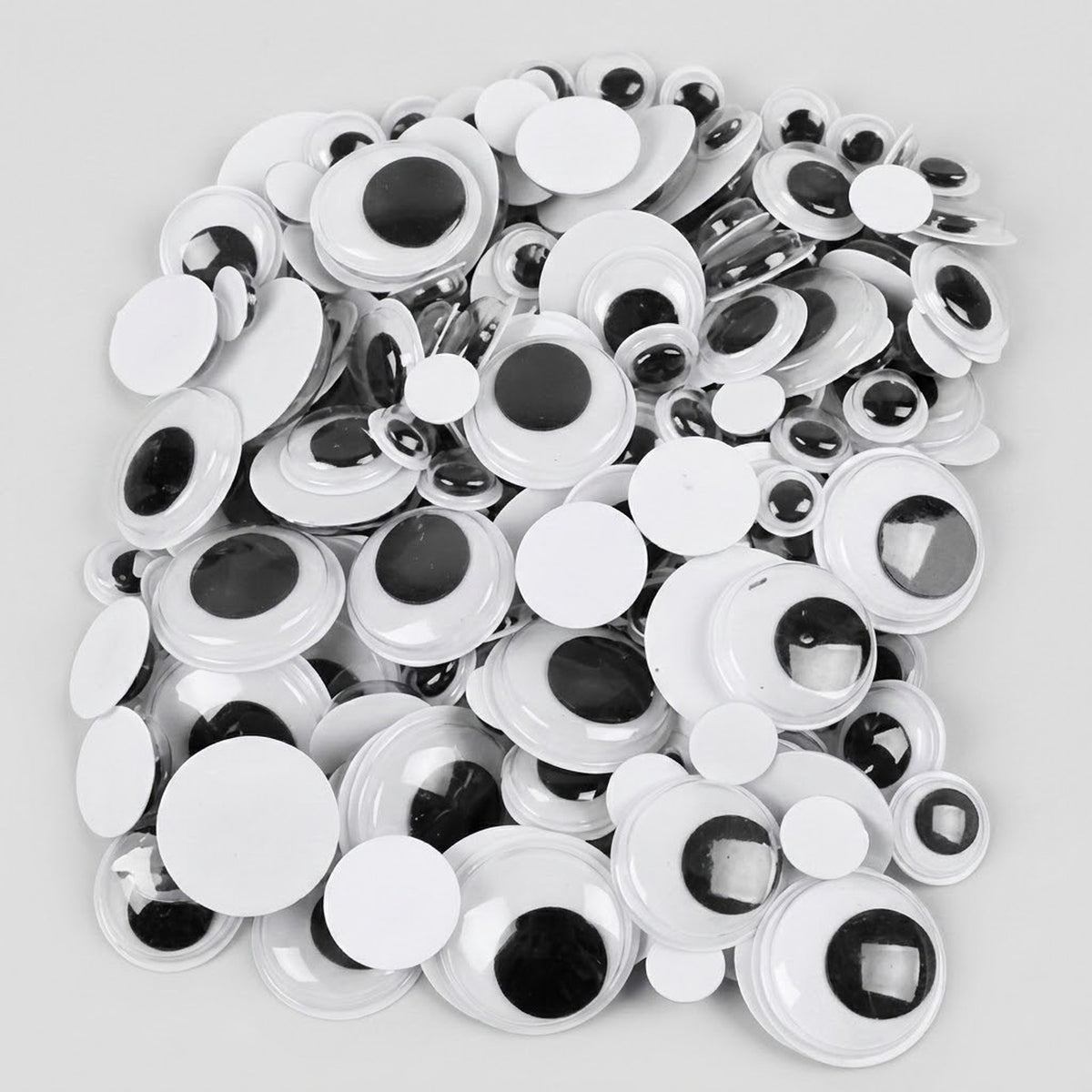 A pile of white plastic novelty googly eyes with black plastic pupils, photographed on a light gray background.