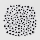 A pile of novelty plastic googly eyes in various sizes, featuring white circular bodies with black centers, arranged on a light gray background.