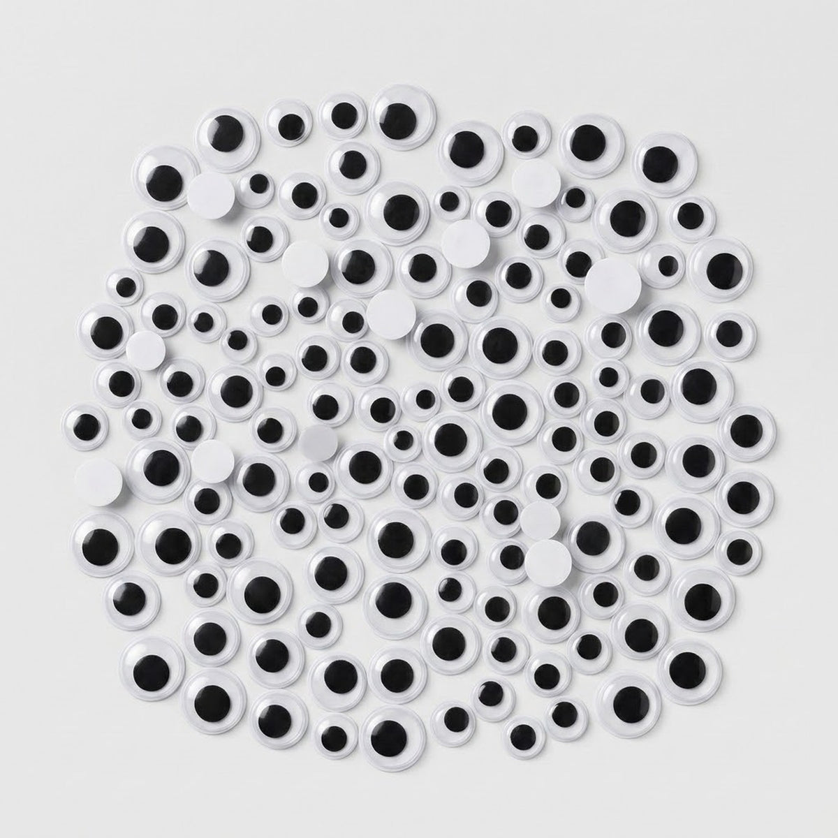 A pile of novelty plastic googly eyes in various sizes, featuring white circular bodies with black centers, arranged on a light gray background.