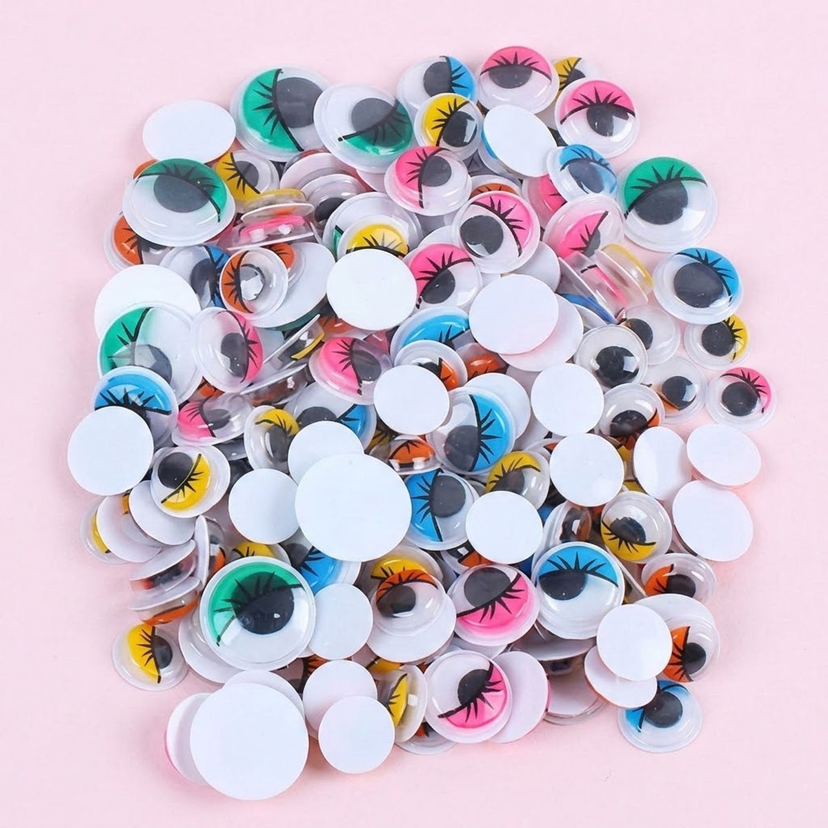 Multicolor plastic googly eyes with black pupils, eyelash details, and white backs form a pile on a pale pink background.