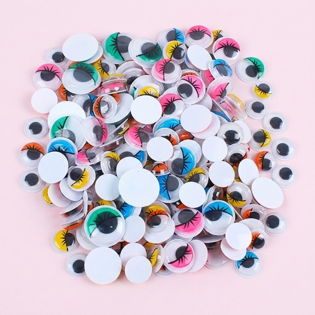A pile of colorful novelty googly eyes with white circular heads and multicolored iris details, scattered on a light pink background.