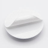 A plastic googly eye rests backing-side up with its white adhesive liner partially peeled away against a white background.