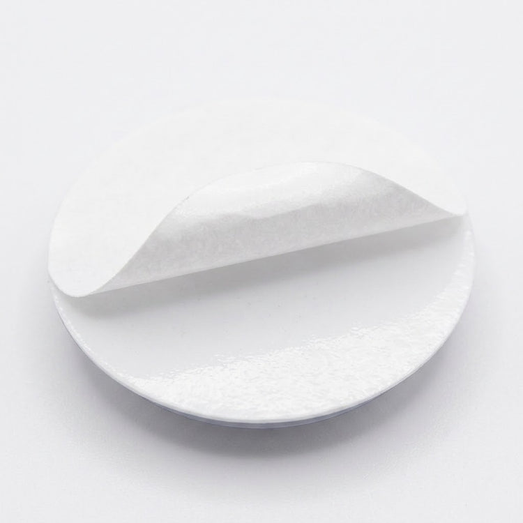 A plastic googly eye rests backing-side up with its white adhesive liner partially peeled away against a white background.