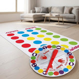 A party game mat with colorful circles and a round spinner with a red pointer rests on a wooden living room floor.
