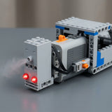 A gray plastic model exhaust sprayer emits mist beside two glowing red lights on a building block assembly on a gray tabletop.