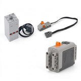A gray plastic model exhaust sprayer, battery case, orange-accented switch, and black connecting cables are arranged separately on a white background.