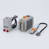 A gray plastic model exhaust sprayer with two red lenses sits beside a ribbed battery case and orange-control switch on white.