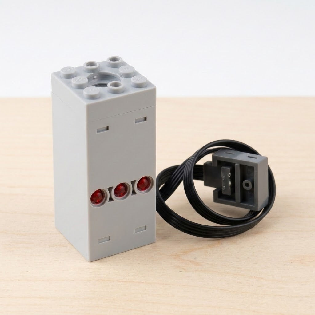 A gray plastic model exhaust sprayer with three red circular details stands beside a coiled black cable on pale wood.