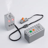A gray model exhaust sprayer emits mist with two glowing red lights beside a battery case and orange-control switch on white.