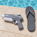 A gray and white water pistol sits beside a flip-flop on poolside stone to show its compact scale.