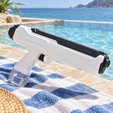 White manual water squirt gun rests on a beach towel beside the water in summer light.