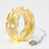A coiled roll of warm white LED fairy string lights on a thin wire, with a white USB connector cable visible on a clean white background.