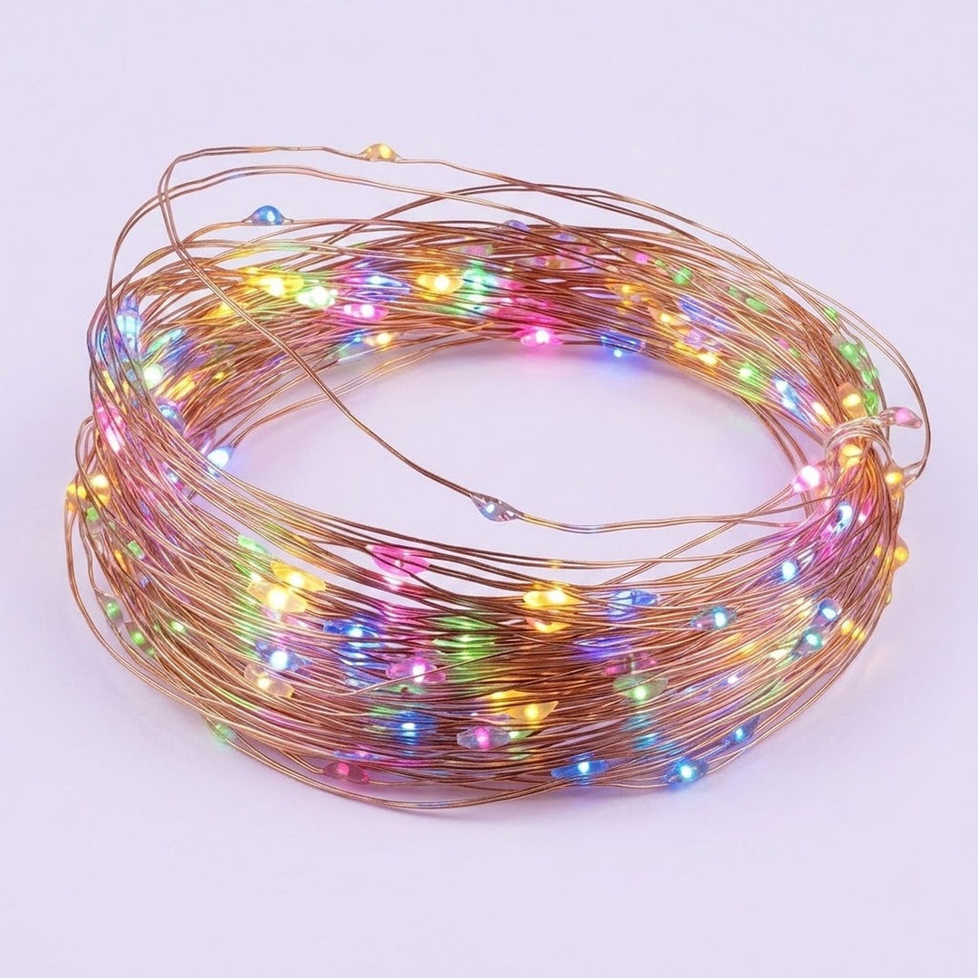 A coiled bundle of copper wire fairy string lights glowing with multicolor LED bulbs, set against a plain light purple background.