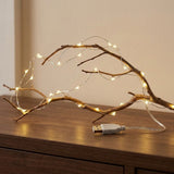 Warm white string light follows a bare branch on a wooden console, with its attached USB lead and connector visible.