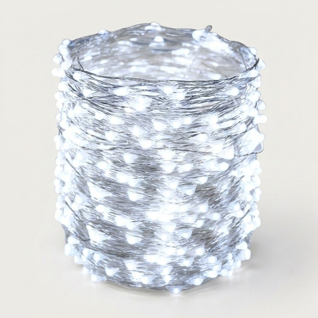 A roll of white LED fairy string lights wrapped tightly around a cylindrical form, photographed against a plain light beige background.
