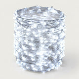 A roll of white LED fairy string lights wrapped tightly around a cylindrical form, photographed against a plain light beige background.