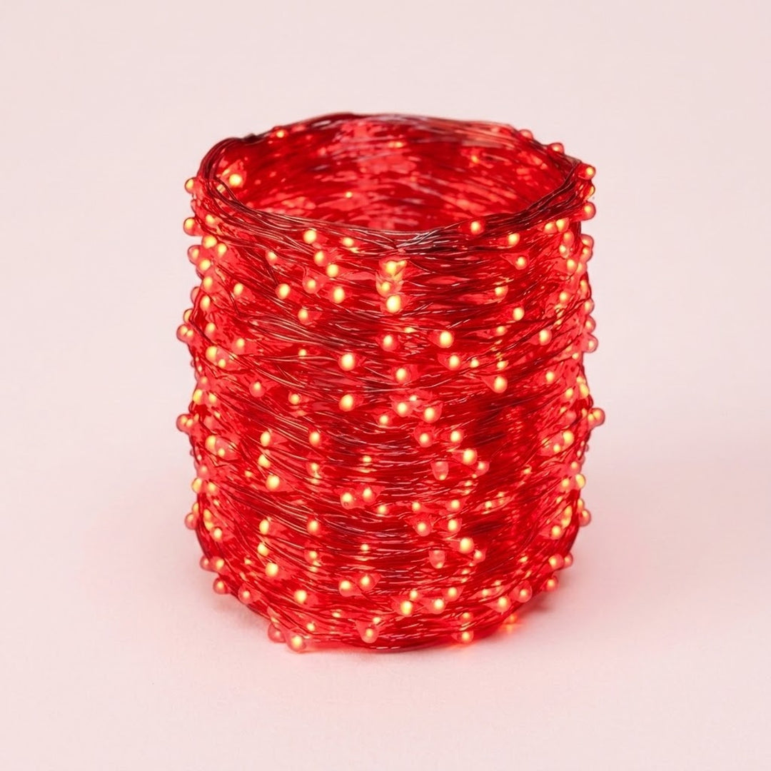A coil of red LED fairy string lights glowing with a warm red-orange light, photographed on a clean light pink background.