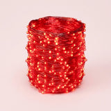 A coil of red LED fairy string lights glowing with a warm red-orange light, photographed on a clean light pink background.