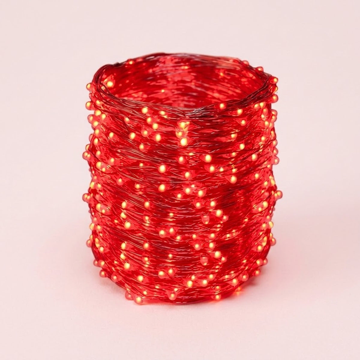 A coil of red LED fairy string lights glowing with a warm red-orange light, photographed on a clean light pink background.