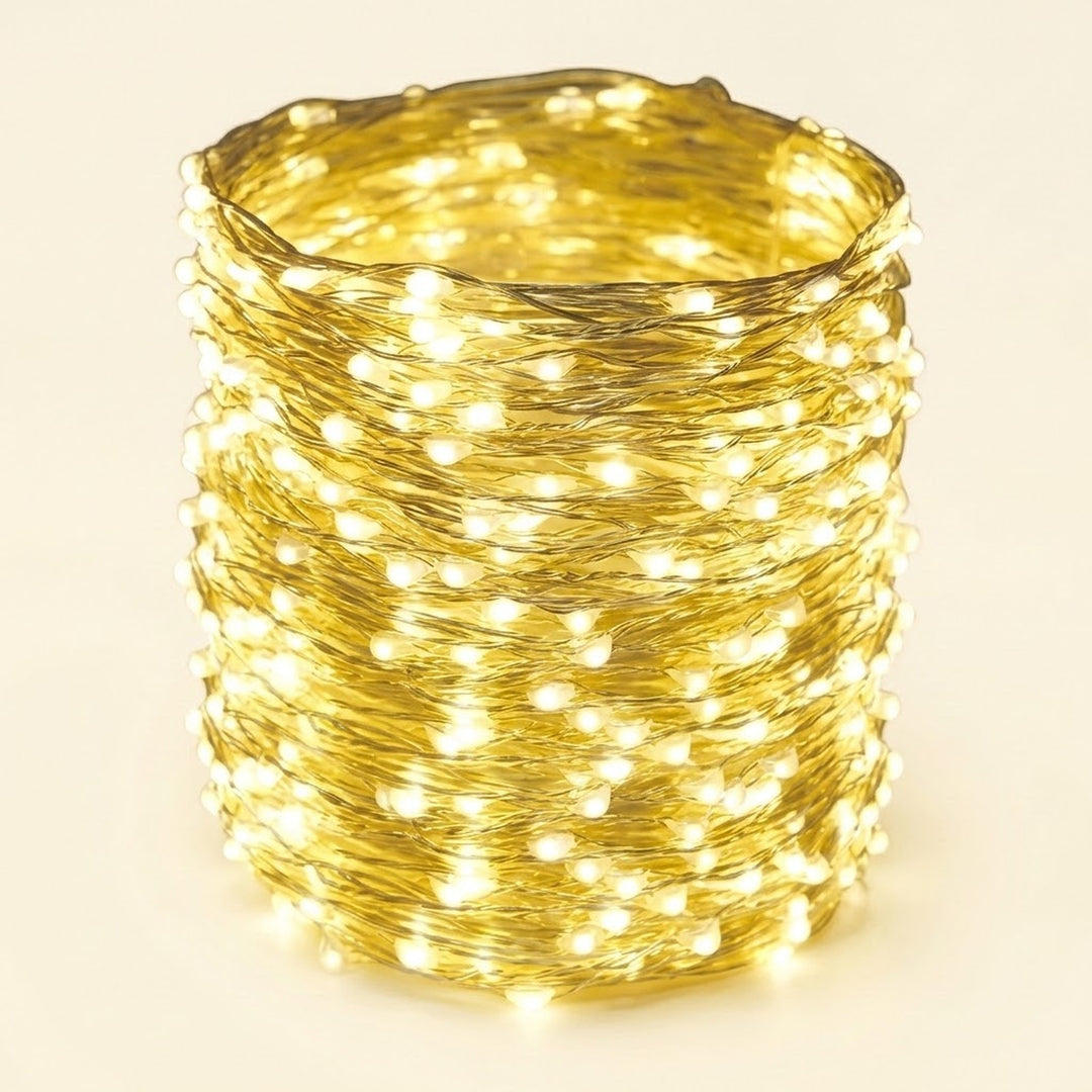 A coiled bundle of warm white LED fairy string lights wrapped tightly together, glowing brightly against a plain light beige background.