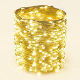 A coiled bundle of warm white LED fairy string lights wrapped tightly together, glowing brightly against a plain light beige background.