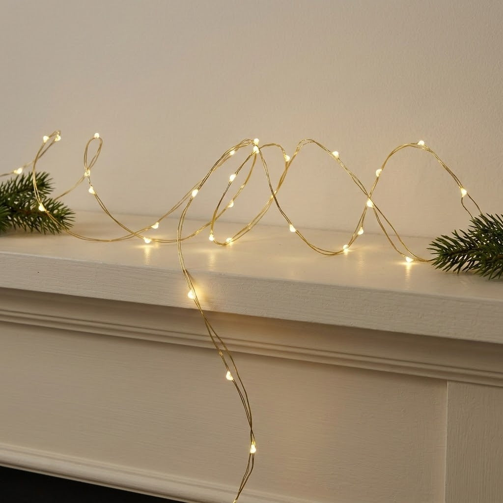 Warm white LED fairy string lights draped in loops across a white mantelpiece, flanked by green pine branches on both sides.