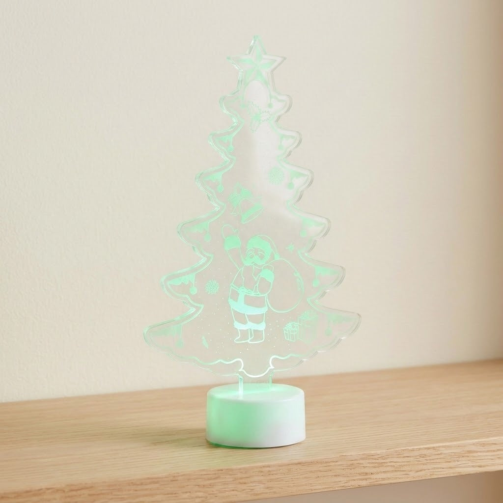 A glowing Christmas tree-shaped LED night light with a Santa Claus design, resting on a light wood surface against a plain beige wall.