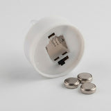 The white base of a mini Christmas night light showing its open battery compartment beside three silver coin batteries.