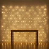 Warm white curtain string lights hanging in a grid pattern on a wall, casting a golden glow over a wooden table and floor.