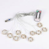 An LED curtain light has coiled clear strands, a connected USB controller and a white remote arranged on a white background.