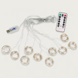 An unlit curtain light spreads clear strands into circular coils, with a USB connector and white remote on an off-white background.