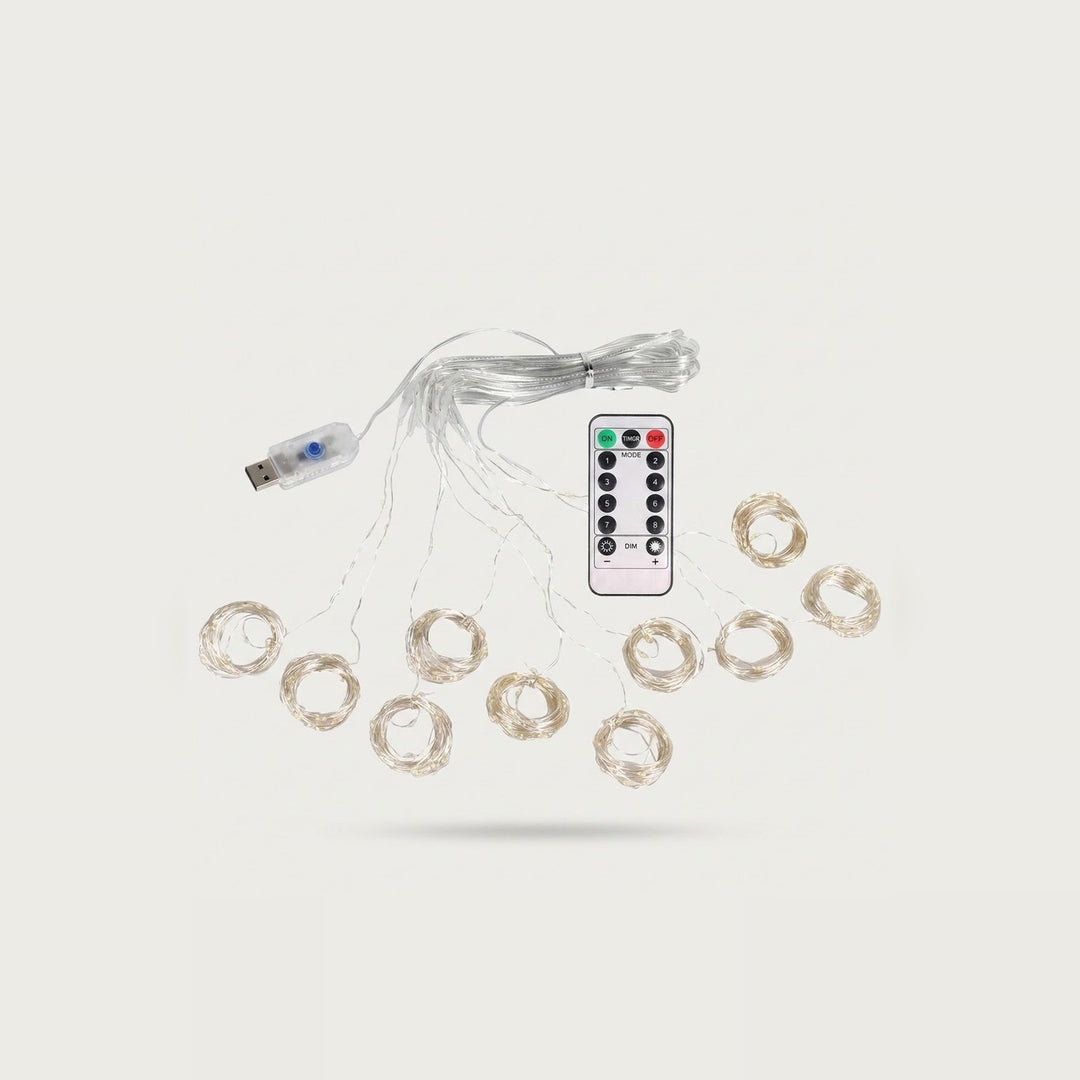 An unlit curtain light with clear coiled strands surrounds a white remote, with a USB connector at left against an off-white background.