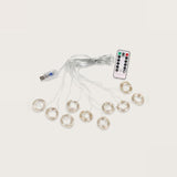 An unlit curtain light with clear wiring fans into circular coils beside a USB connector and white remote on a beige background.