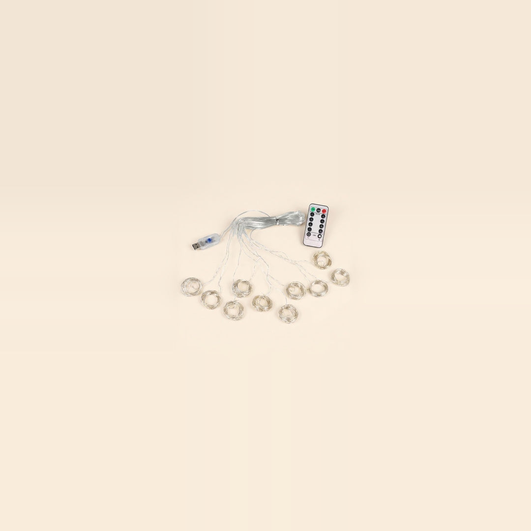 An LED curtain light with coiled clear strands, a USB controller and a white remote sits centered against a spacious cream background.