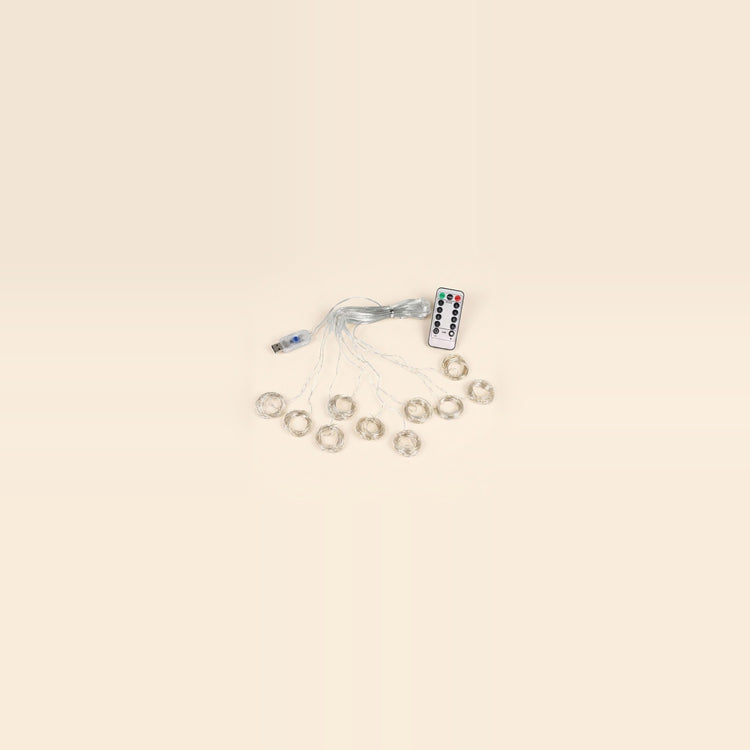 An LED curtain light with coiled clear strands, a USB controller and a white remote sits centered against a spacious cream background.