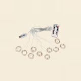 An LED curtain light with coiled clear strands, a connected USB controller and a white remote is arranged on a cream background.