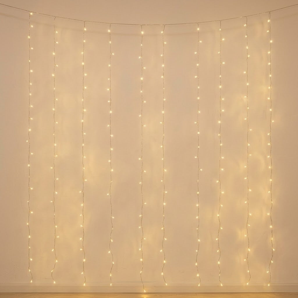 Warm white curtain string lights hanging in vertical strands against a plain beige wall, casting a soft glow.