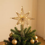 A gold wire star tree topper with warm white string lights, displayed on top of a decorated green Christmas tree with gold ornaments in an indoor setting.