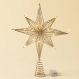 Gold layered eight-point star tree topper with glowing LEDs, spiral mounting base, and battery compartment against a cream background.